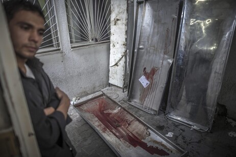 A Palestinian man stand next to bloodied gurneys in the morgue of the Kamal Adwan hospital