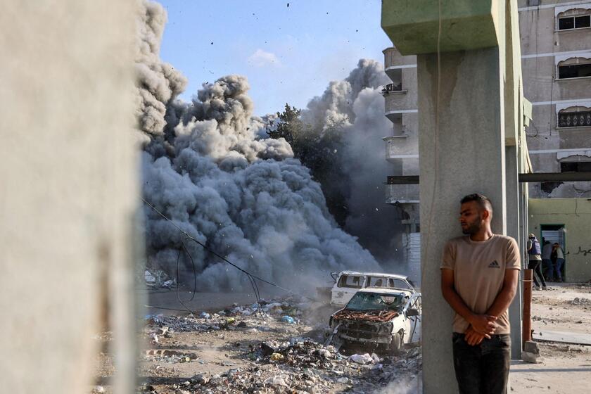 Um homem se esconde atrás de uma coluna enquanto uma explosão propaga fumaça e poeira em Gaza